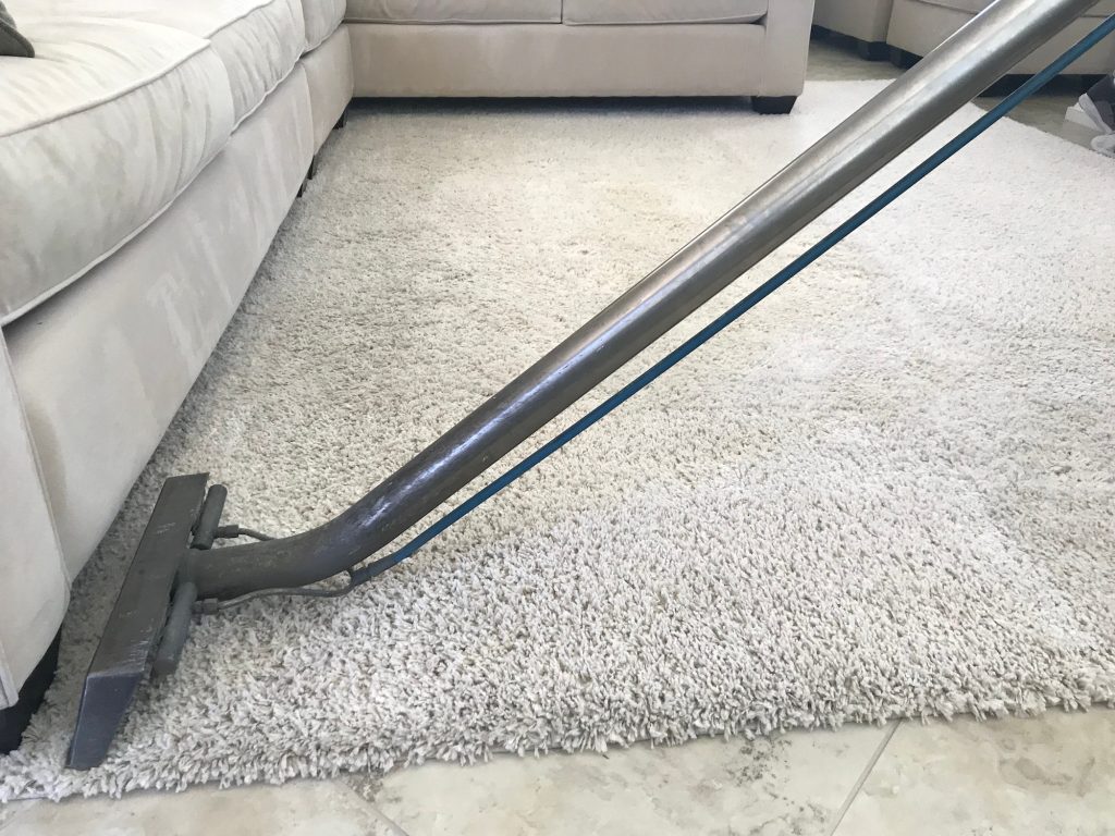 A man is using a shampooer to steam clean a white rug