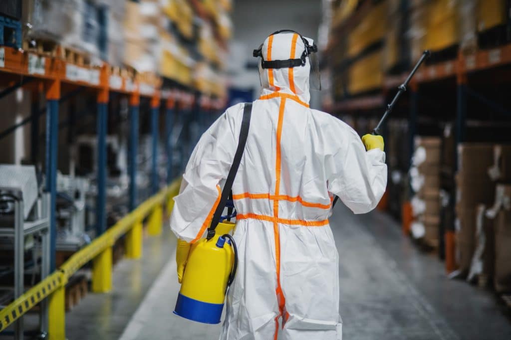 Rear view of man worker with protective suit disinfecting industrial factory with spray gun