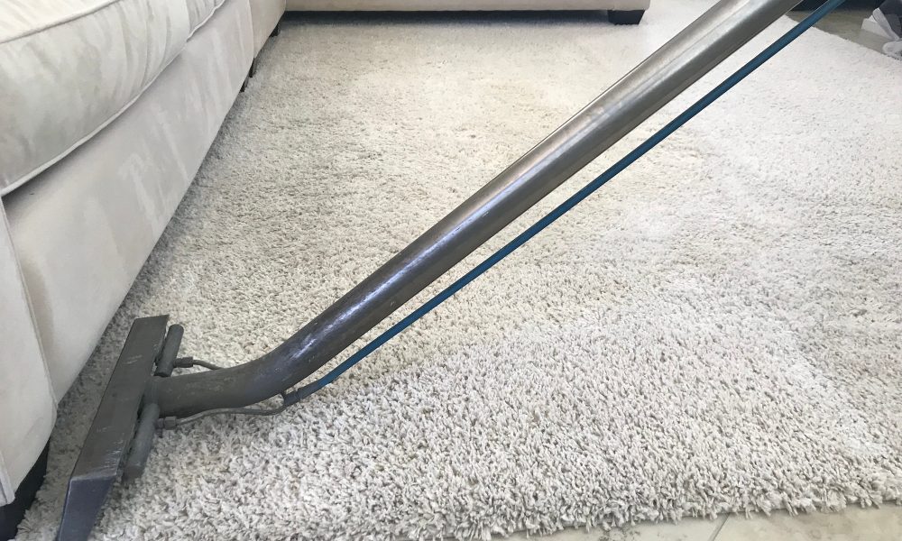 A man is using a shampooer to steam clean a white rug