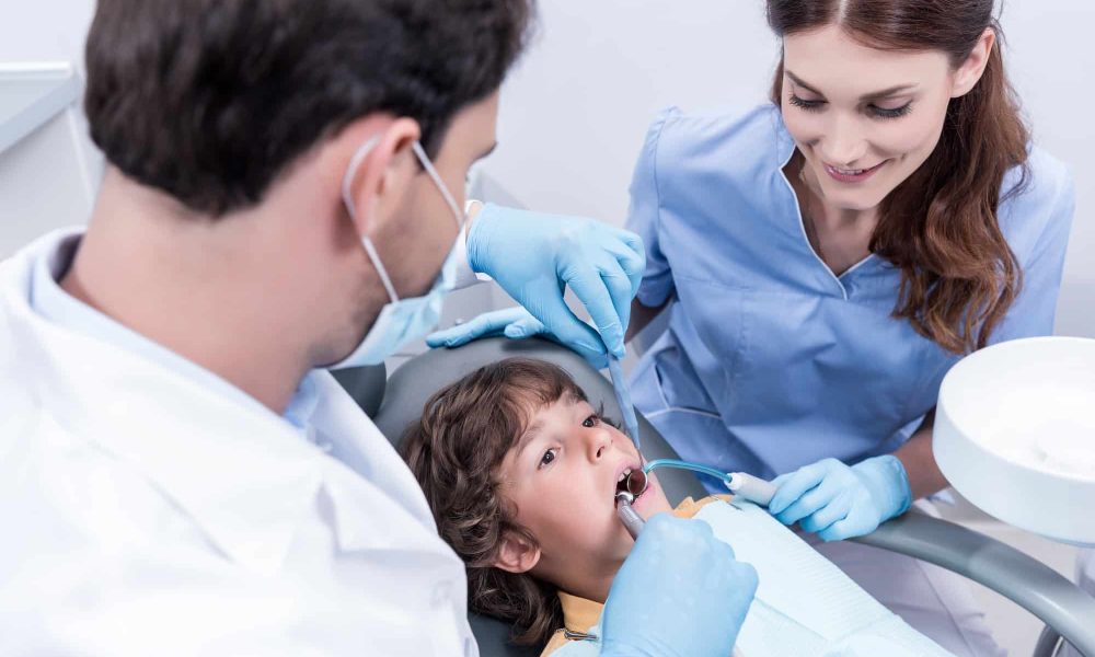 dentists treating teeth of little patient in dentist chair in hospital